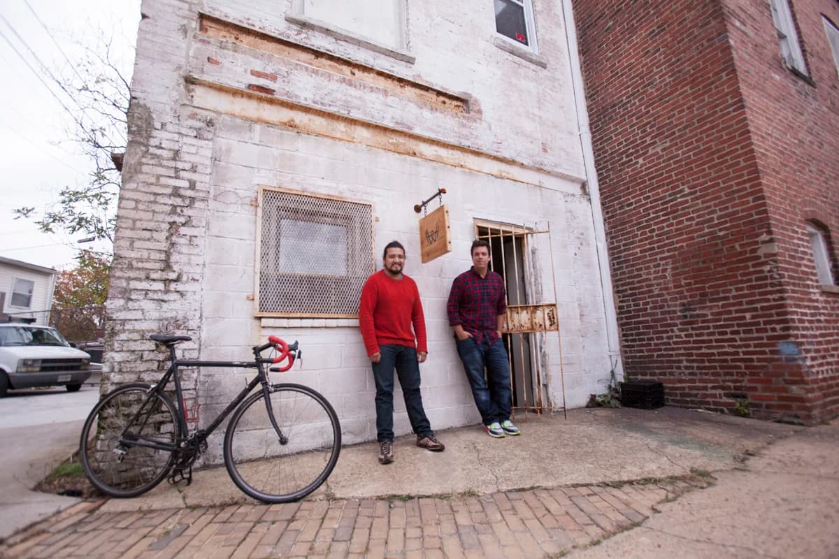 Abe and Tj standing in the doorway of the early shared studio, brick row house, bike against the wall.