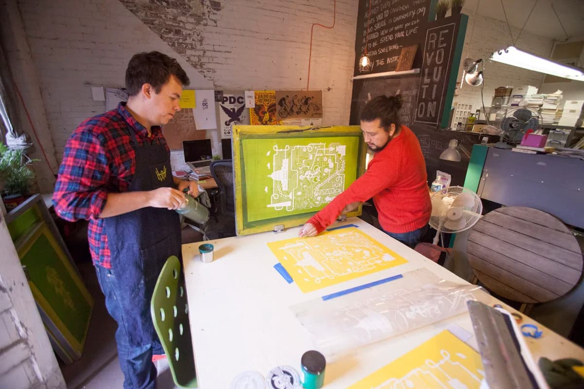 Two of the studio team registering a yellow Artcrank poster against a green emulsion screen.