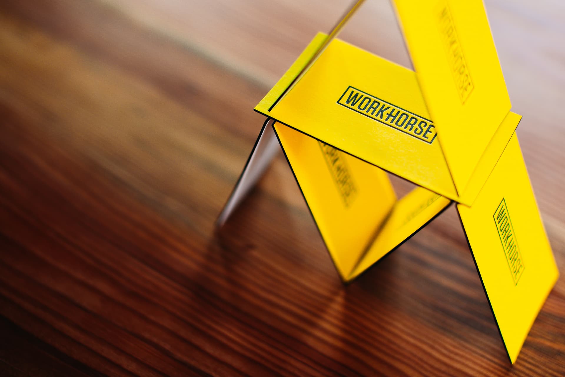 A stack of yellow letterpressed Workhorse business cards on a walnut tabletop.