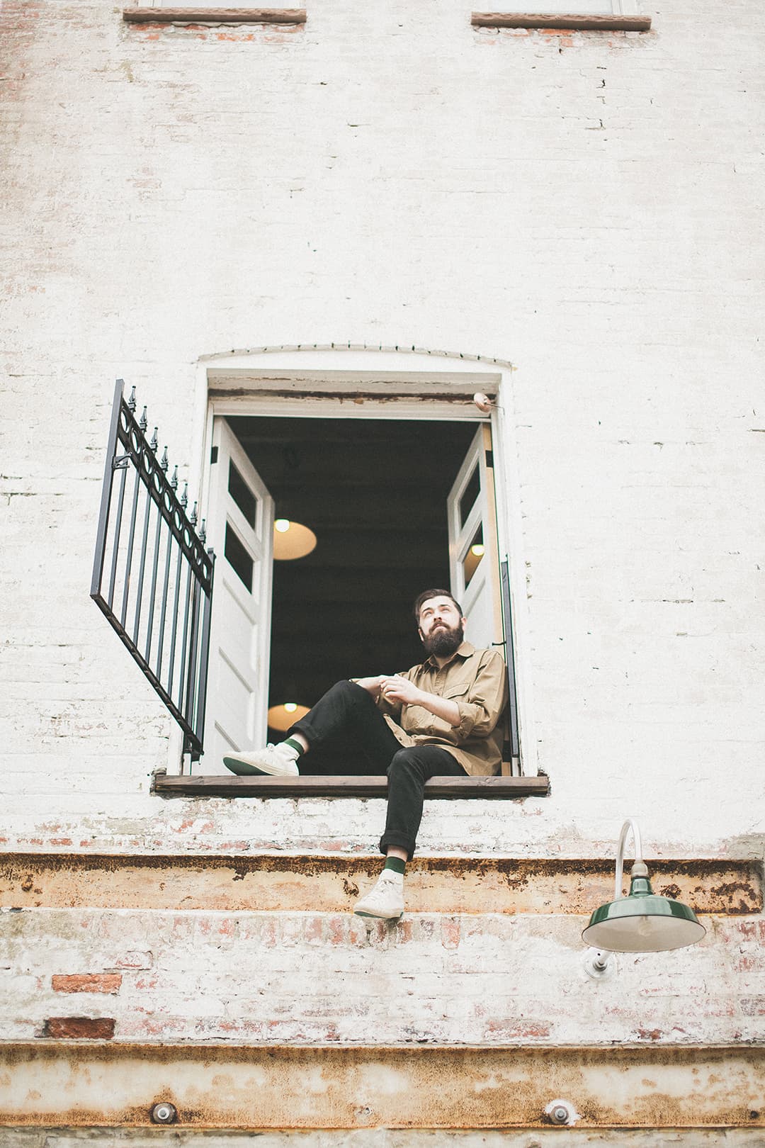 Greg sitting in the second-floor window of the carriage house, against painted brick.