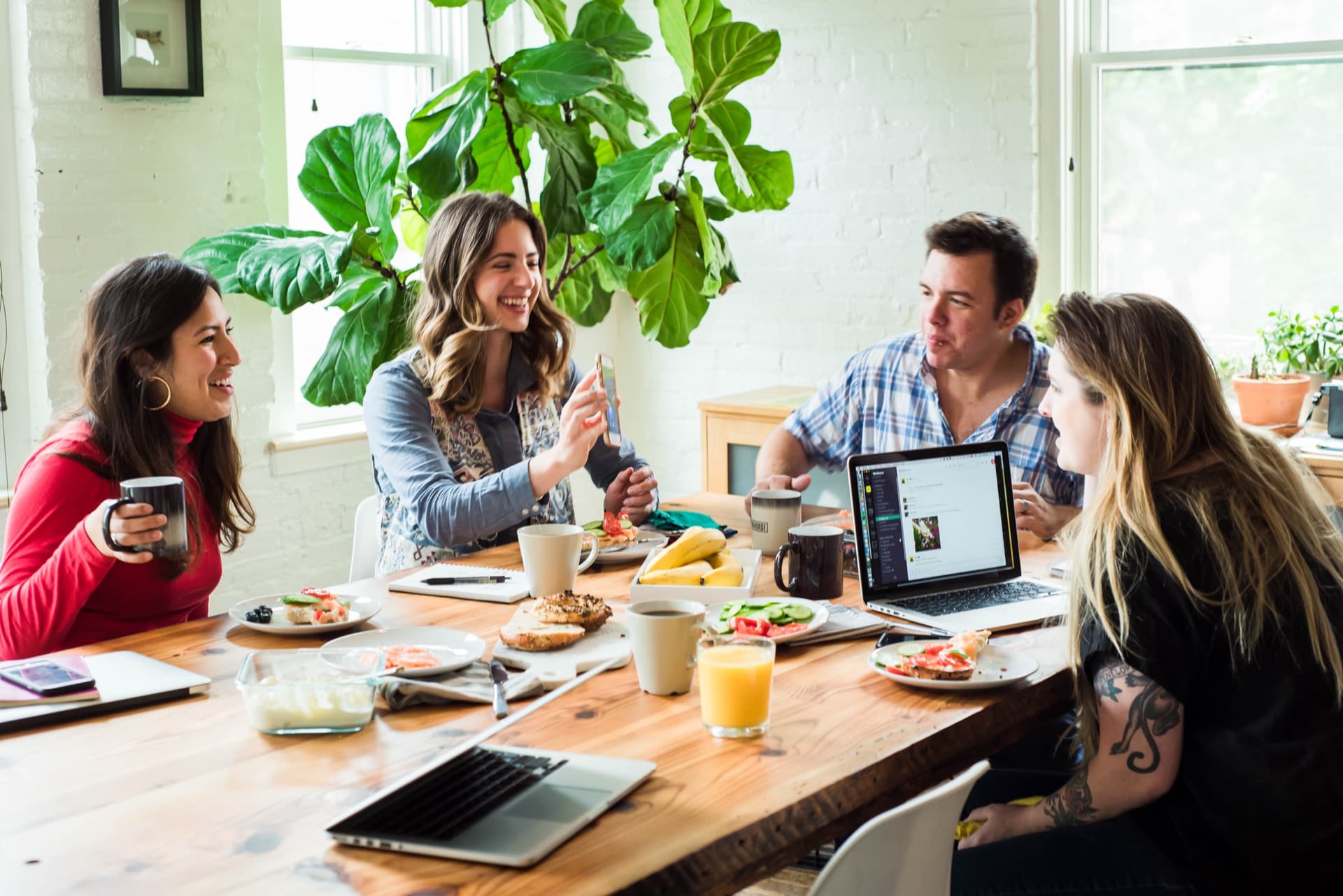 The Workhorse team at the studio kitchen table, sharing breakfast, laptops open, fiddle leaf fig behind them.