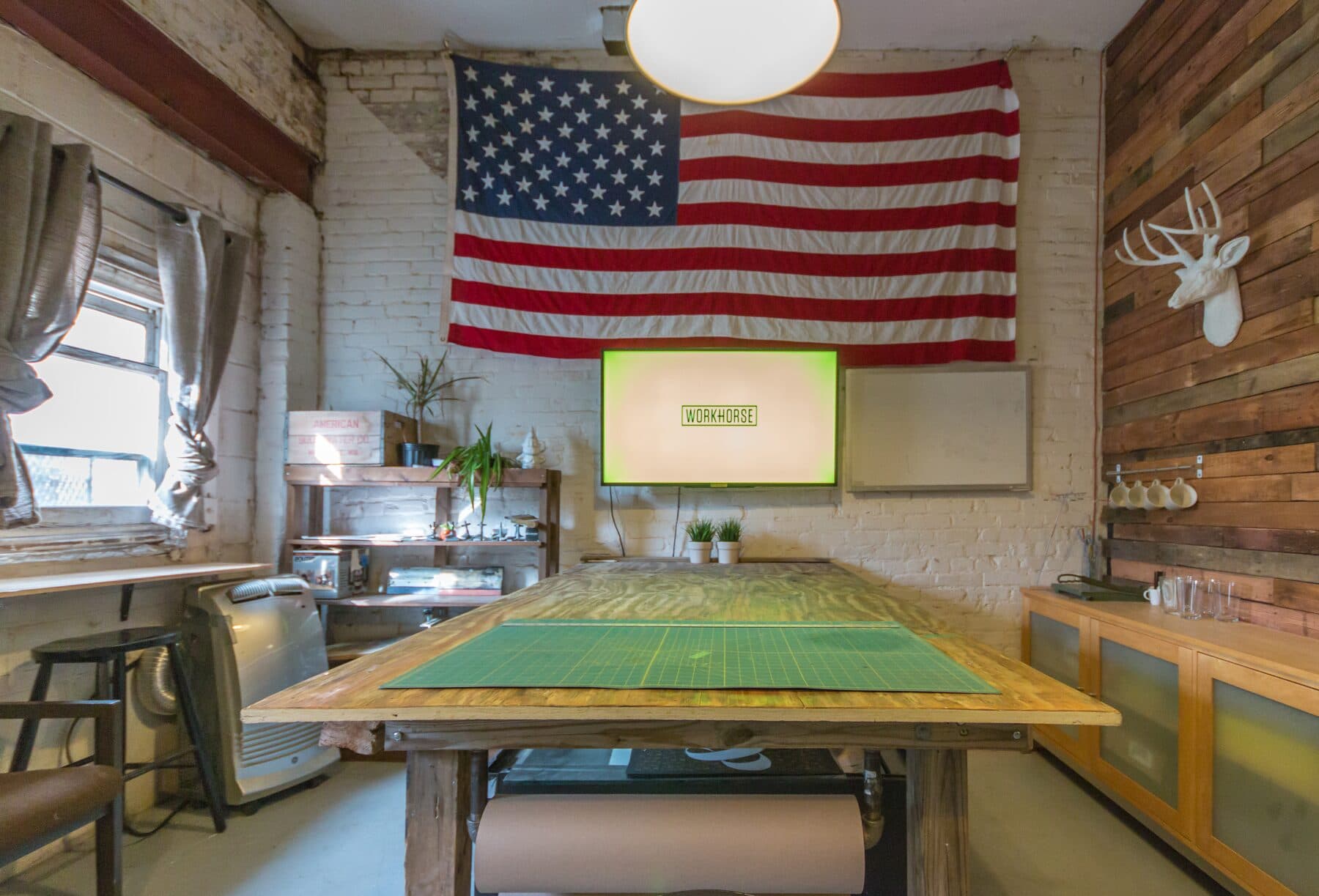 The studio work table covered in proofs, monitors, and a fiddle leaf fig.