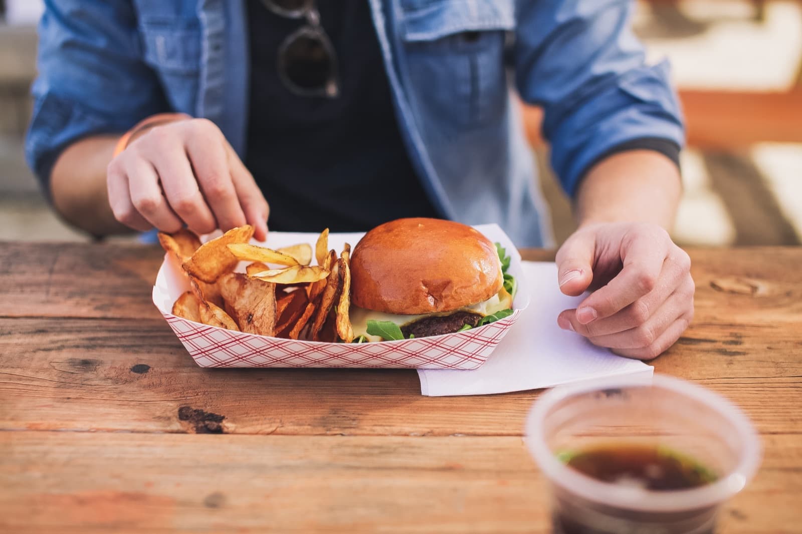 Hands reaching for a brioche-bun burger and home-cut fries served in a red checkered paper boat at the DC Design Week closing party.