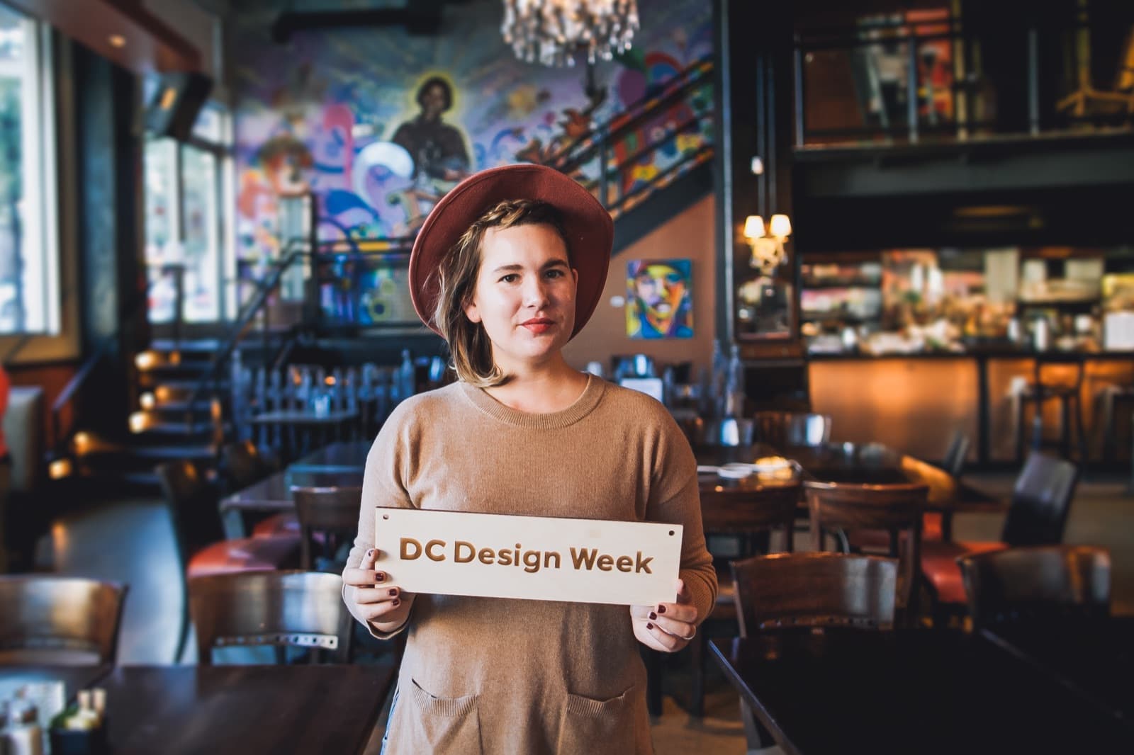 Portrait holding a wooden DC Design Week sign inside a colorful bar at A Creative DC.