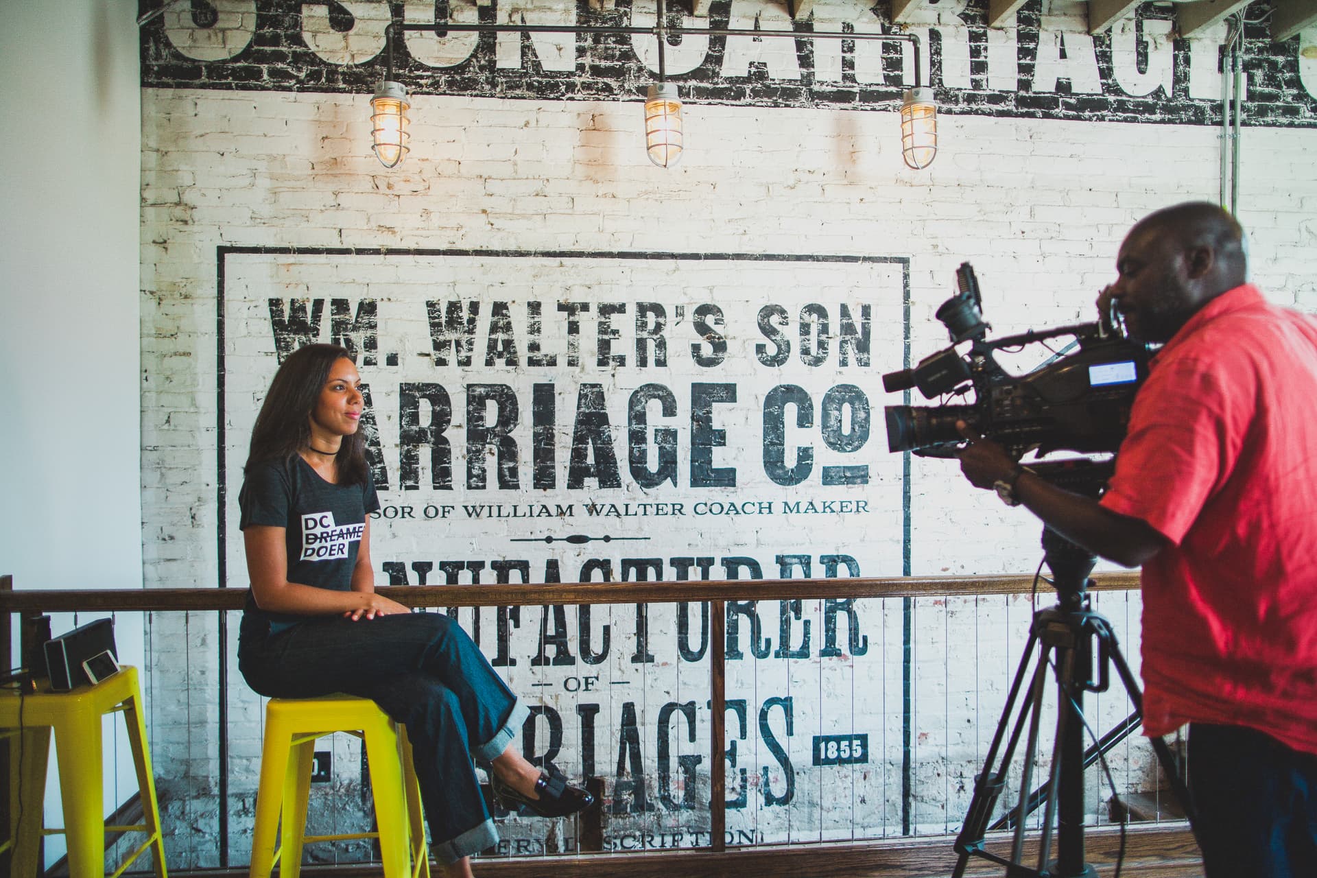Camera crew filming an interview against the Walter’s Son Carriage Co. ghost-sign wall.