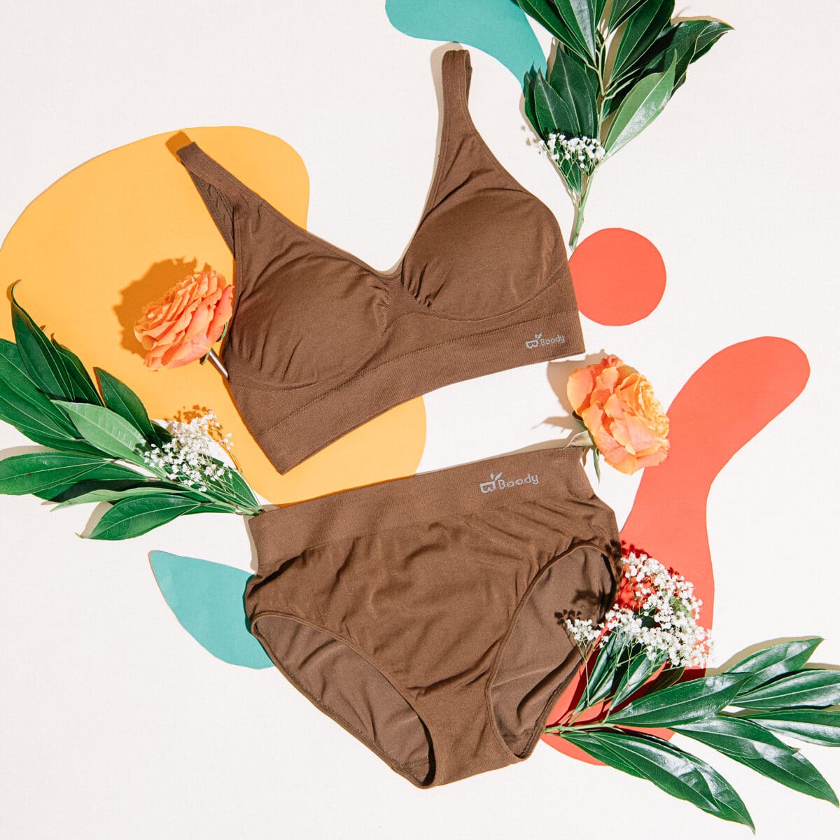 A bra and brief laid out with a peach rose and dark leaves