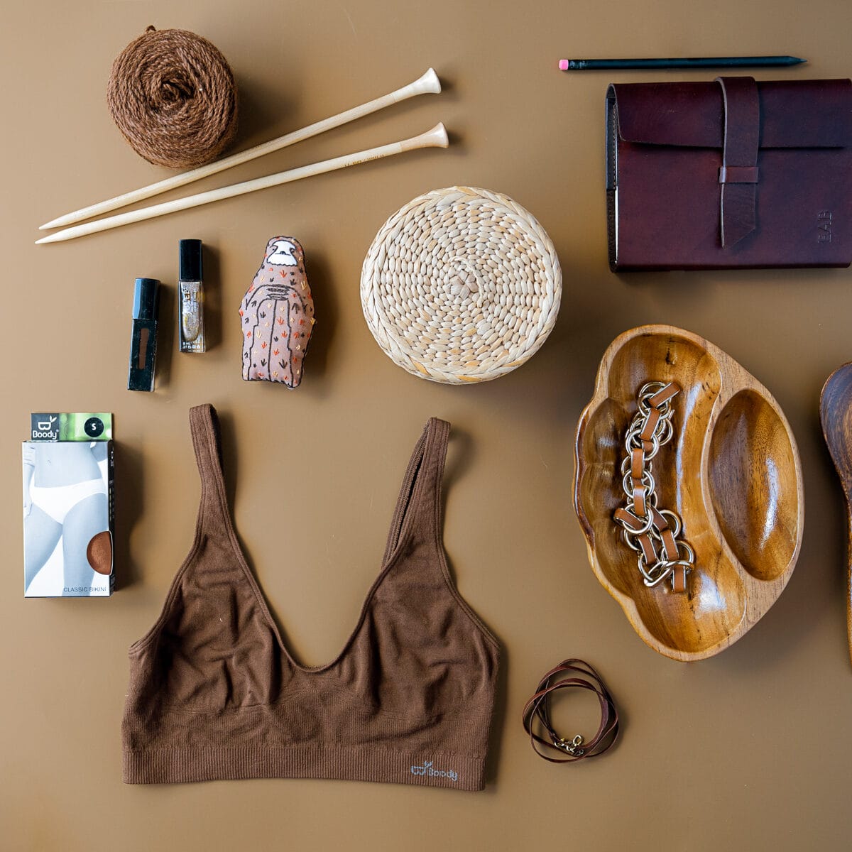 Flatlay on tan: a Boody bra laid out with knitting yarn, a leather notebook and a woven dish