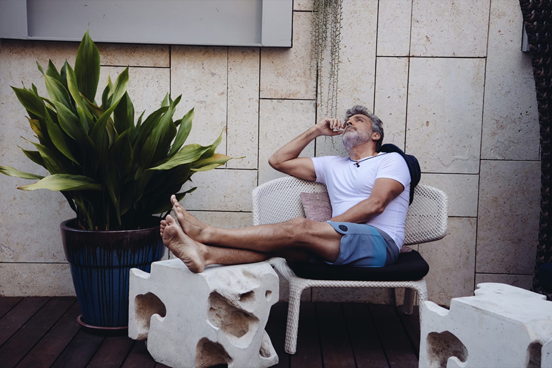 Man on a lounger among planters with a glass at his lips
