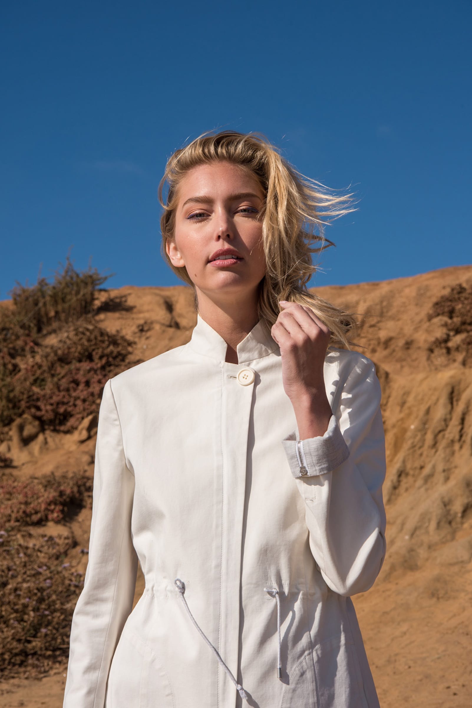 Woman in a cream coat against blue sky and dune