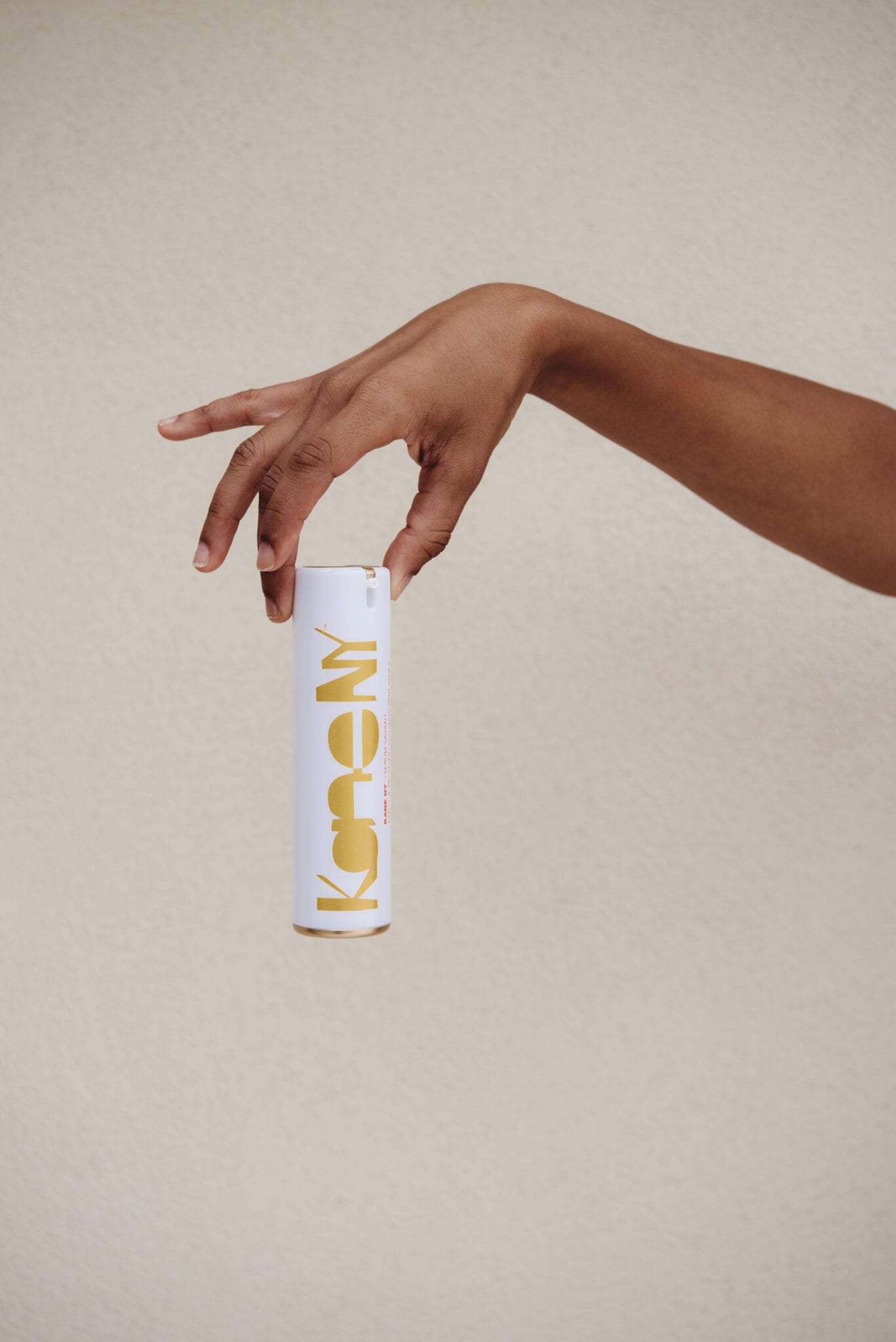 A hand balancing the tube upright against a sand-colored wall