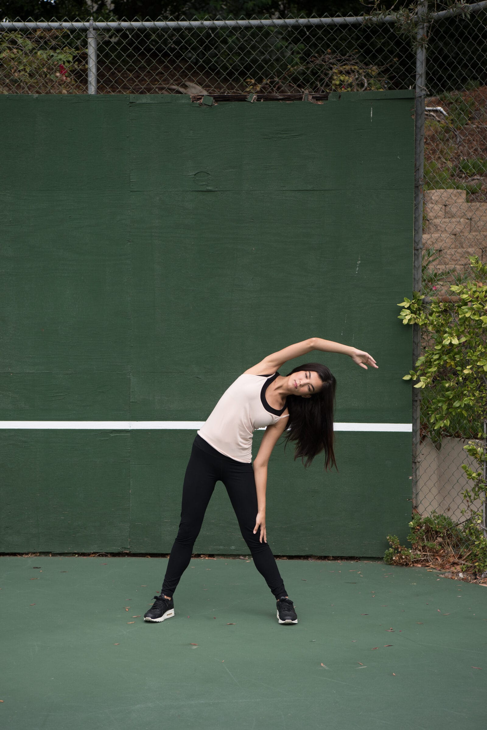 A side bend against the green wall of the tennis court