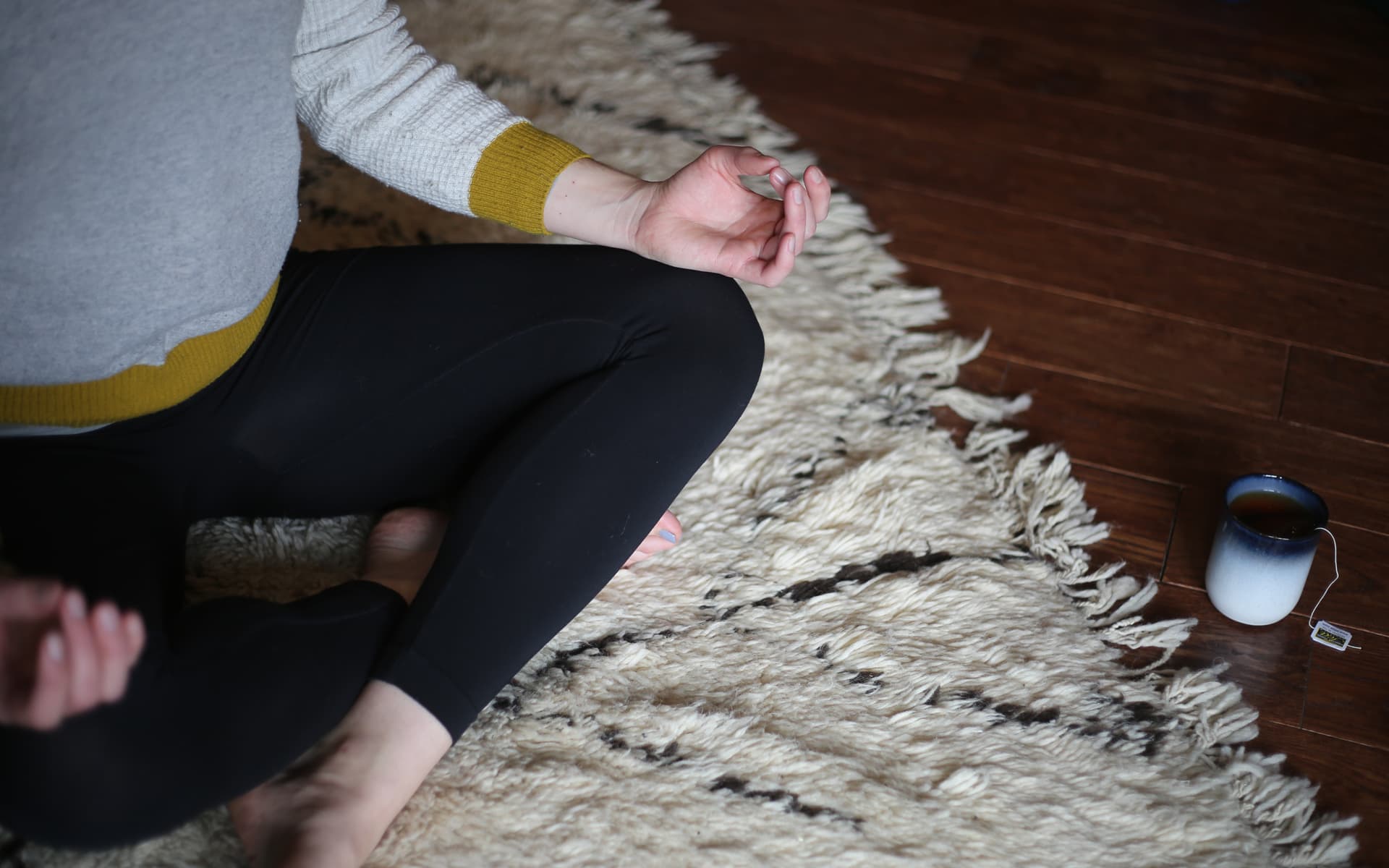 Seated cross-legged on a woven rug in Boody leggings, a mug on the floor beside them