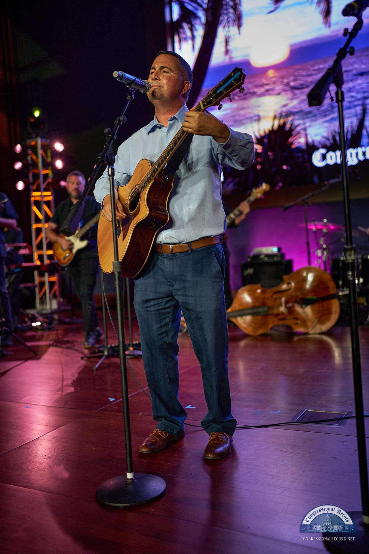 A guitarist singing at the mic in the stage lights