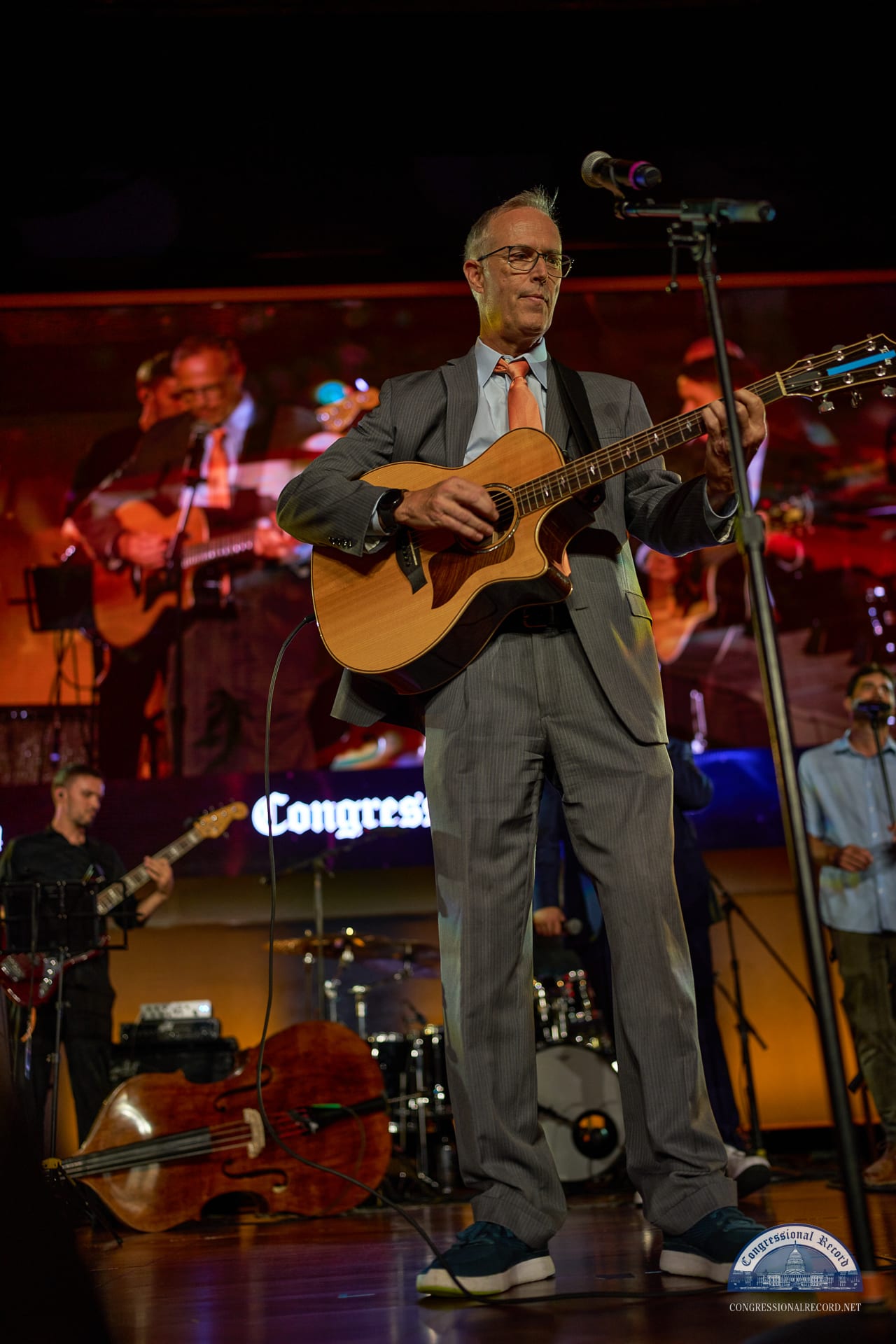 A guitarist in a gray suit at the mic