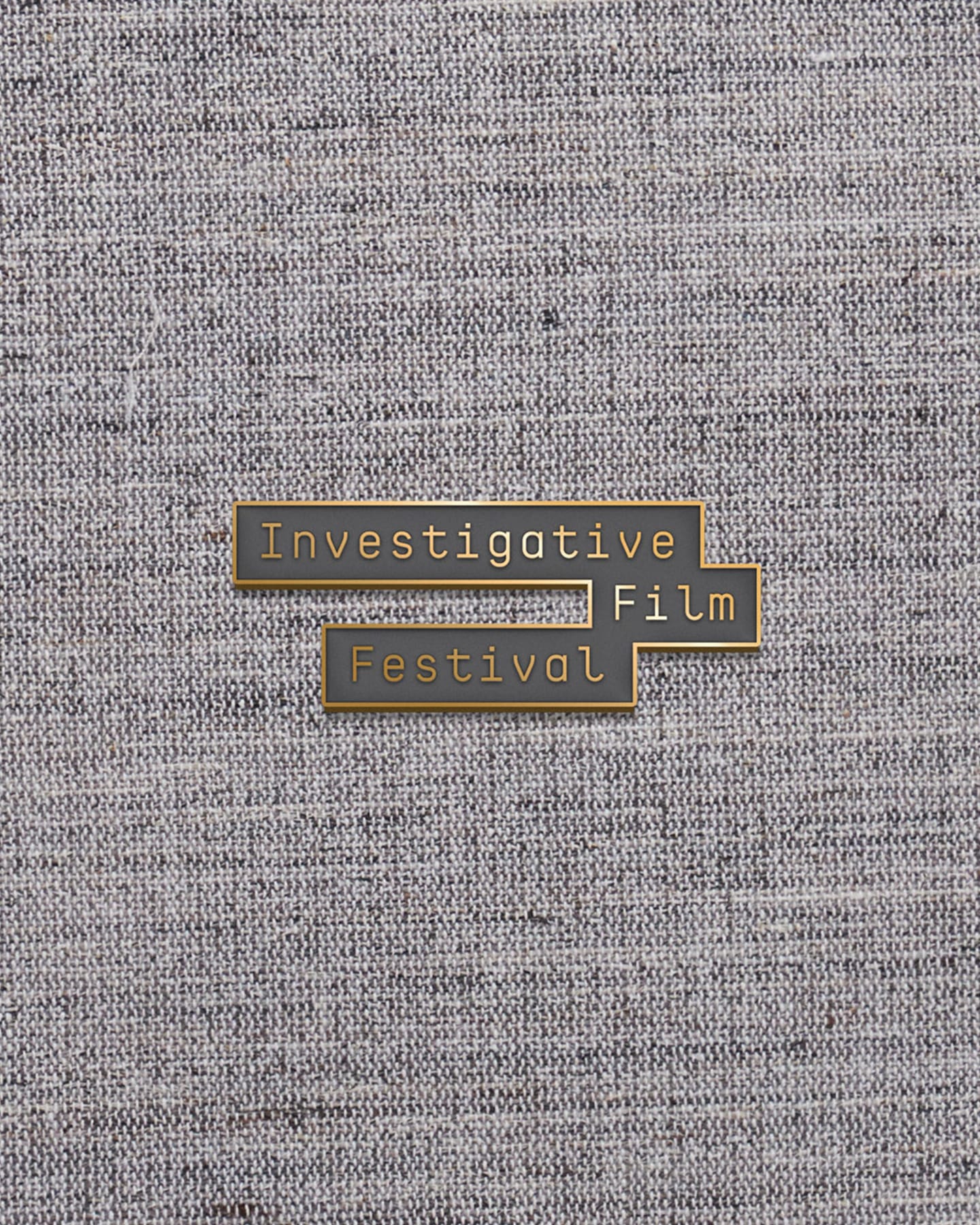 An enamel pin reading Investigative Film Festival on tweed
