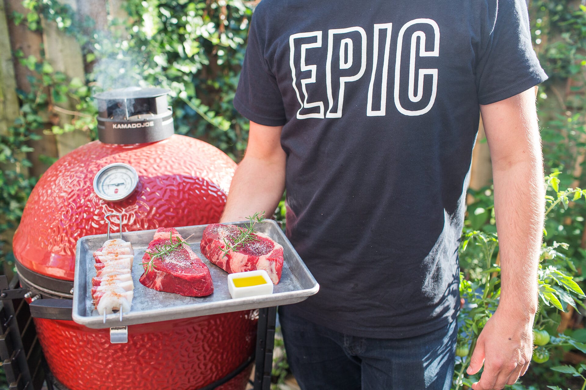 Back of an EPIC tee, a tray of steaks and skewers on the grill shelf