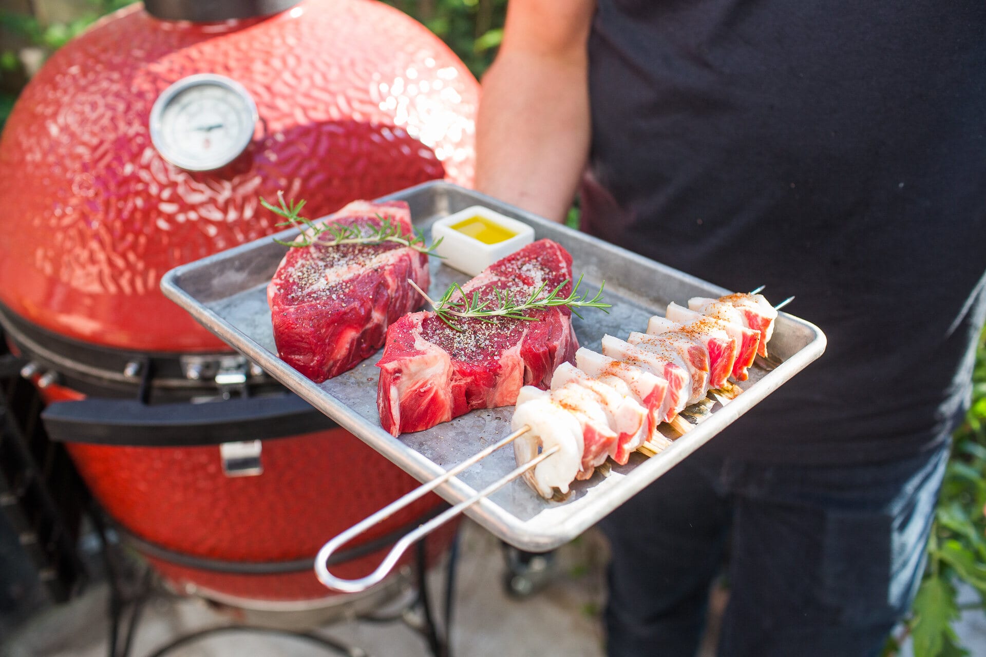 Tray of steaks, skewers, and a yellow cup on the grill side table