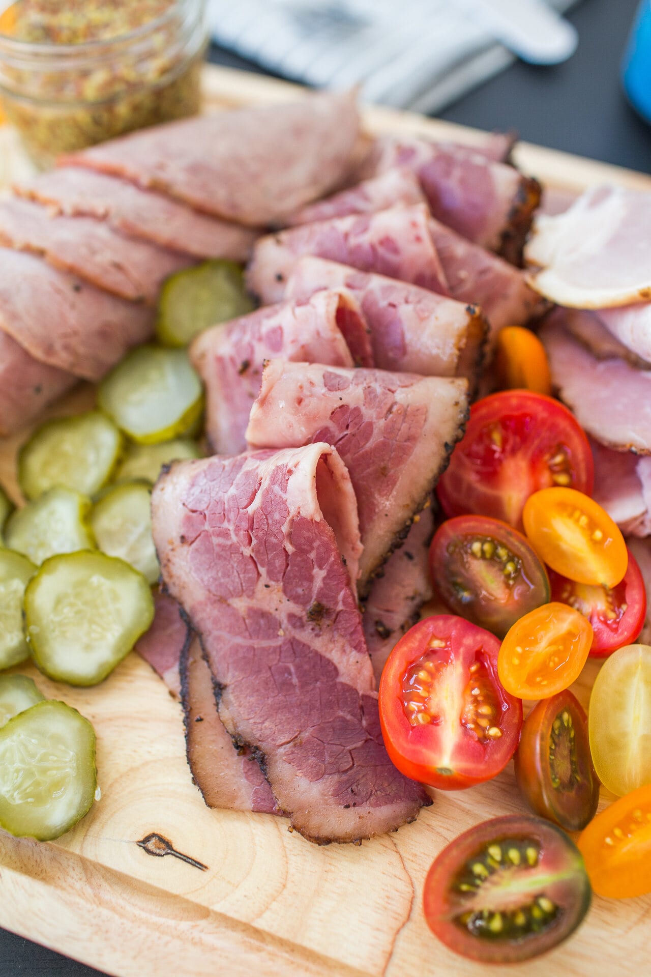 Sliced pastrami with pickles and heirloom tomatoes on a cutting board