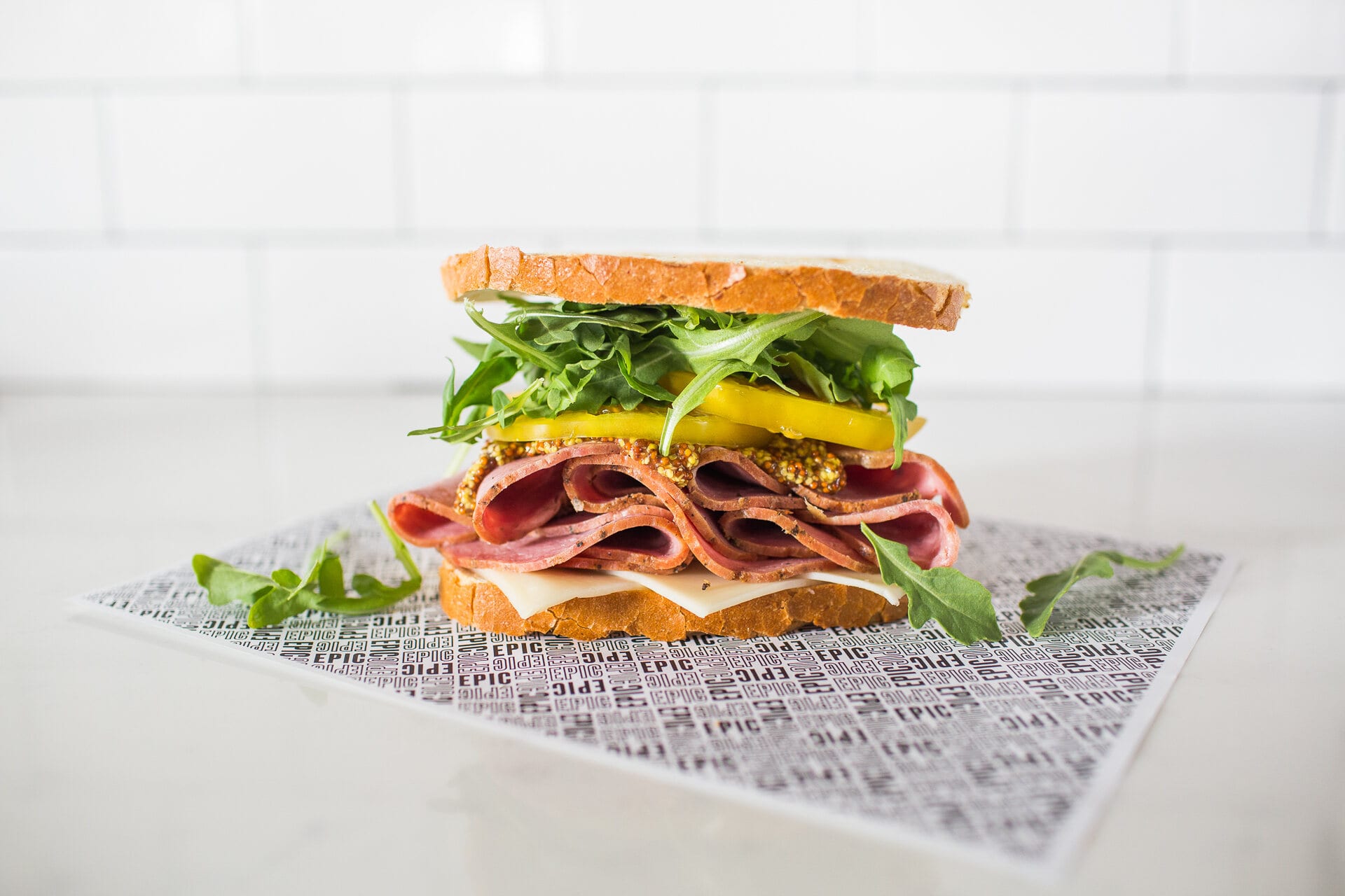 A tall sandwich with greens and pastrami on EPIC paper