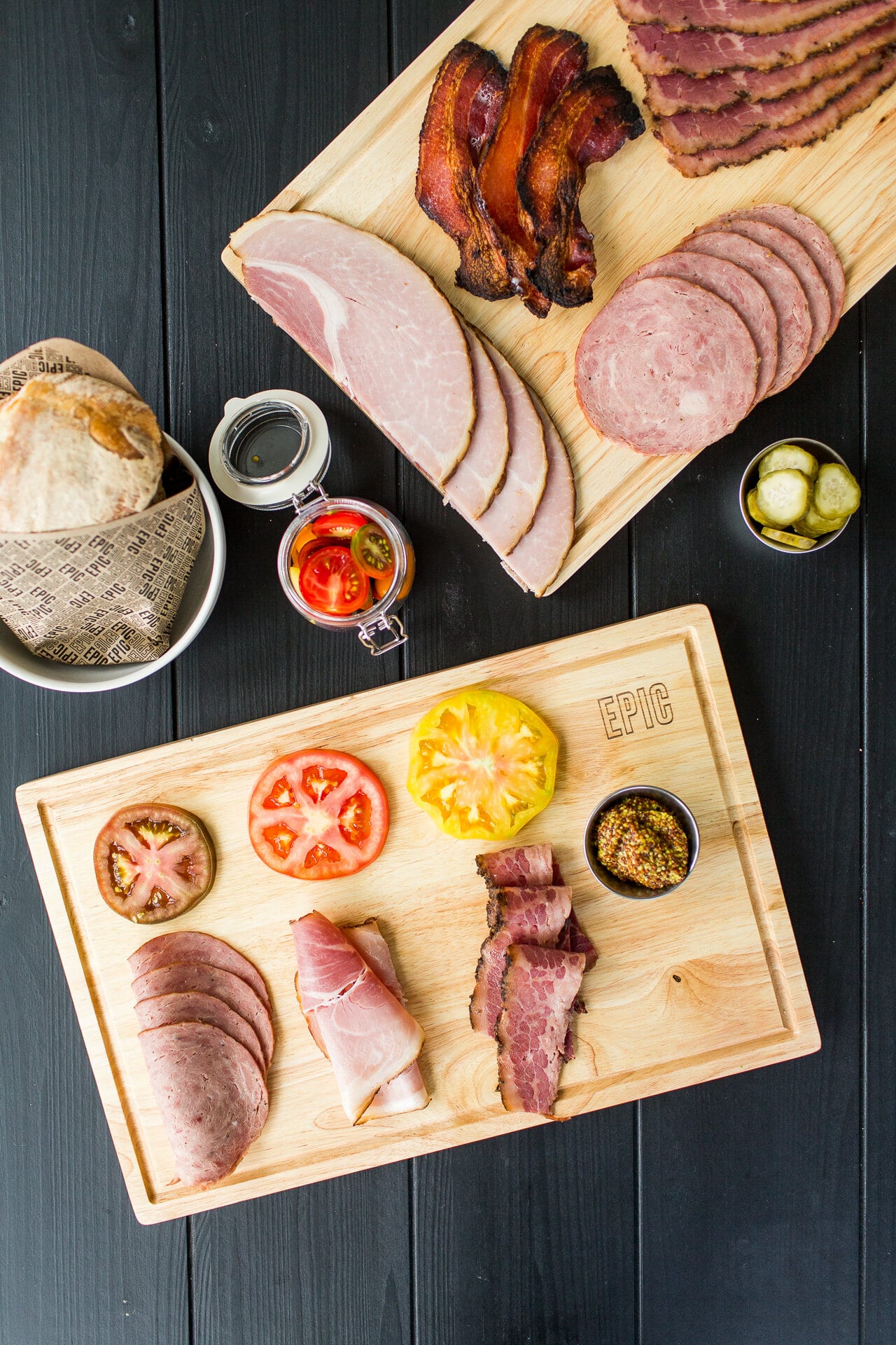 Overhead of an EPIC cutting board with sliced meats, tomato, and mustard