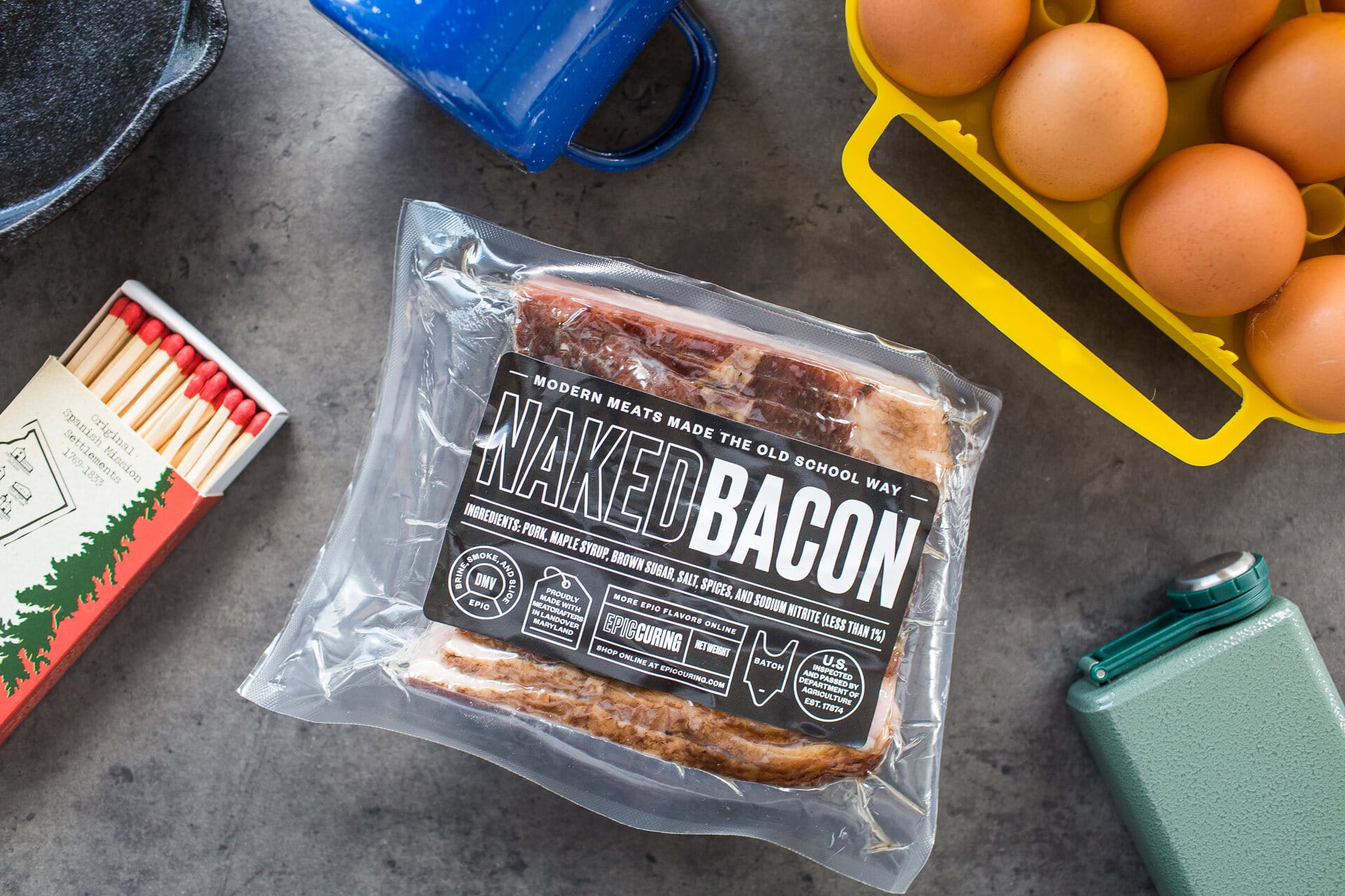 Naked Bacon pack on a slate counter with a blue mug and brown eggs