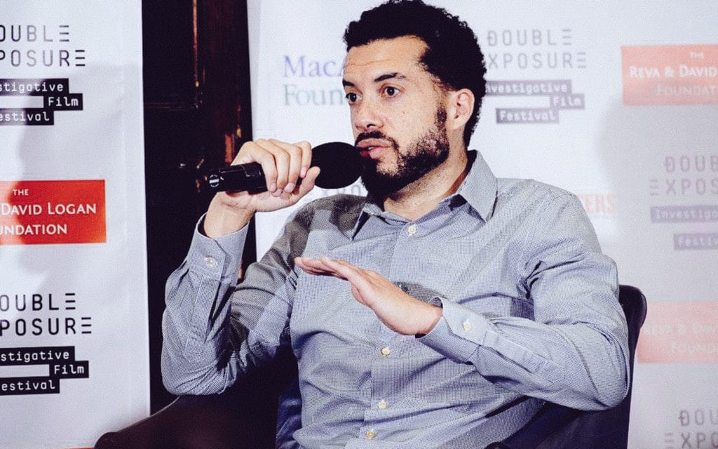 A panelist speaking into a microphone in front of the step-and-repeat